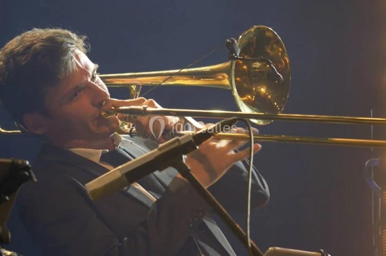 Un musicien en costume joue du trombone sur une scène éclairée par des projecteurs.