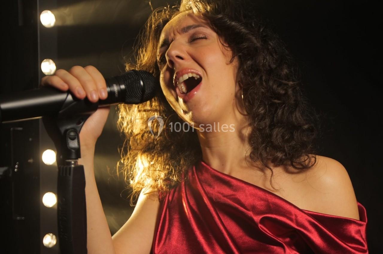 Femme chantant avec passion dans un micro, éclairée par des projecteurs en arrière-plan.