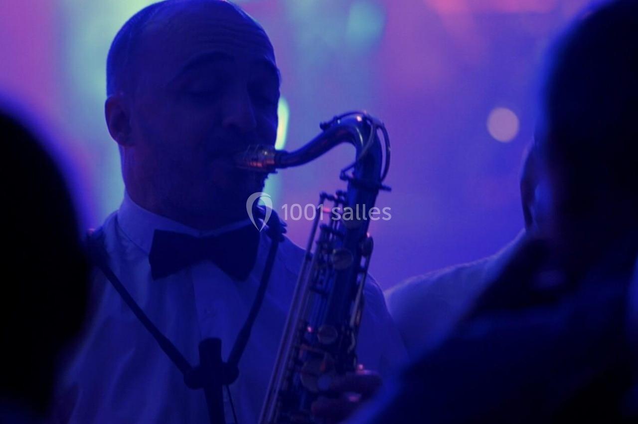 Un musicien joue du saxophone dans une ambiance lumineuse tamisée et colorée, entouré d'un public.