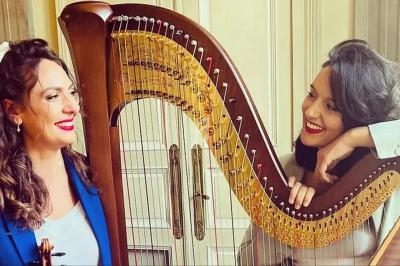 Deux femmes souriantes discutent près d'une harpe dans un intérieur lumineux.