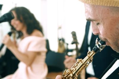 Un musicien joue du saxophone au premier plan, une chanteuse floue en arrière-plan.