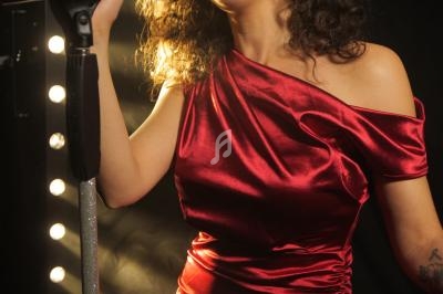 Femme en robe rouge chantant au microphone sous un éclairage de scène.
