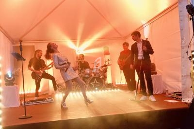 Groupe de musiciens et chanteurs se produisant sur une scène sous une tente éclairée par des lumières chaudes.