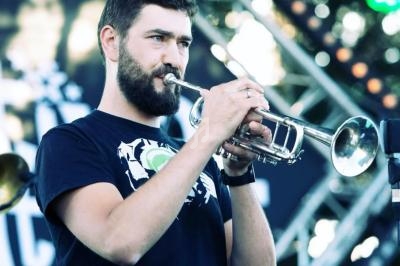 Un homme joue de la trompette sur une scène extérieure, entouré de lumières et d'équipements de concert.