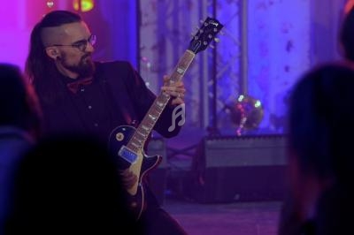 Un musicien joue de la guitare électrique sur scène devant un public dans une ambiance lumineuse colorée.