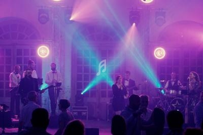 Groupe de musiciens et chanteurs se produisant sur scène dans une ambiance lumineuse violette devant un public.
