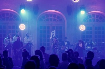 Groupe de musiciens et chanteurs se produisant sur scène devant un public, éclairés par des lumières colorées.