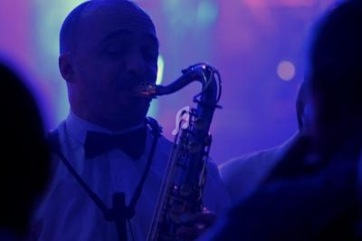 Un musicien joue du saxophone dans une ambiance lumineuse tamisée et bleutée, entouré d'un public.