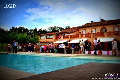 Groupe de personnes rassemblées près d'une piscine devant une grande maison en briques sous un ciel partiellement nuageux.