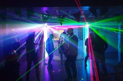 Personnes dansant dans une salle sombre illuminée par des faisceaux lumineux colorés et des lasers.