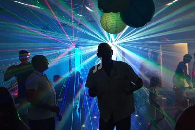 Des personnes dansent dans une salle sombre éclairée par des faisceaux lumineux colorés et des lampions suspendus.