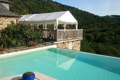 Piscine à débordement avec vue sur une terrasse couverte et un paysage vallonné verdoyant en arrière-plan.