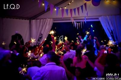 Groupe de personnes célébrant sous une tente, tenant des cierges magiques allumés dans une ambiance festive.