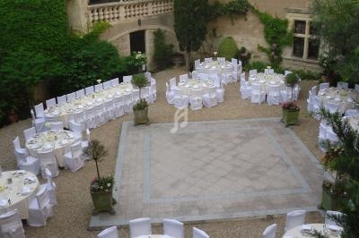 Tables rondes dressées pour un événement dans une cour pavée entourée de murs en pierre et de végétation.