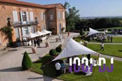 Des invités rassemblés sous des tentes blanches dans la cour d'un grand bâtiment en briques, par temps ensoleillé.
