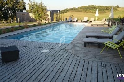 Piscine extérieure entourée de terrasses en bois, avec transats et parasols, dans un cadre naturel verdoyant.