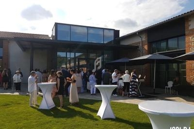 Groupe de personnes rassemblées devant un bâtiment moderne avec grandes baies vitrées, tables hautes et parasols.