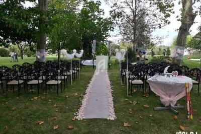 Allée centrale décorée de pétales de fleurs menant à un autel en plein air, entourée de chaises noires.