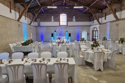 Salle de réception avec tables rondes et rectangulaires décorées, éclairage d'ambiance et murs en pierre apparente.