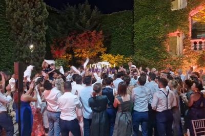 Un groupe de personnes dans une fête en plein air, entouré de murs couverts de végétation et éclairé par des lumières…