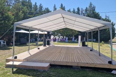 Scène en bois couverte par une structure blanche, installée en extérieur avec des arbres en arrière-plan.