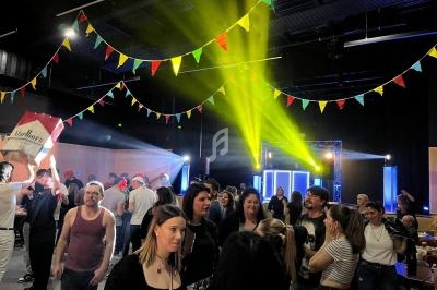 Des personnes dansent et discutent sous des guirlandes colorées dans une salle éclairée par des jeux de lumière.