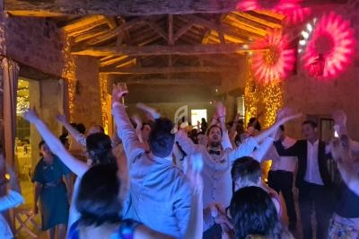 Groupe de personnes dansant sous des lumières colorées dans une salle en pierre avec un plafond en poutres apparentes.
