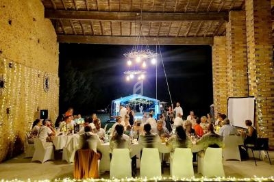 Groupe de personnes dînant sous une structure ouverte décorée de guirlandes lumineuses, avec une tente éclairée en arrière…