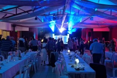Salle de réception avec des invités dansant sous des jeux de lumière bleus, tables dressées au premier plan.