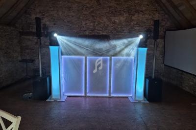 Installation lumineuse avec projecteurs et enceintes dans une salle en pierre, écran blanc en arrière-plan.