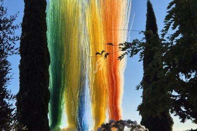 Jets de fumée colorée s'élevant dans le ciel lors d'un événement en plein air, entouré d'arbres et de spectateurs assis.