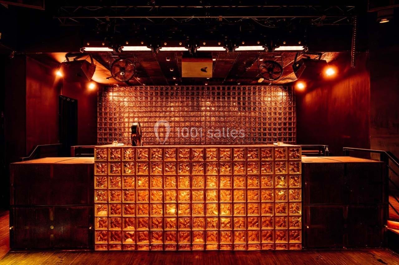 Scène de club avec un mur en briques de verre illuminé et une personne derrière une table de mixage.