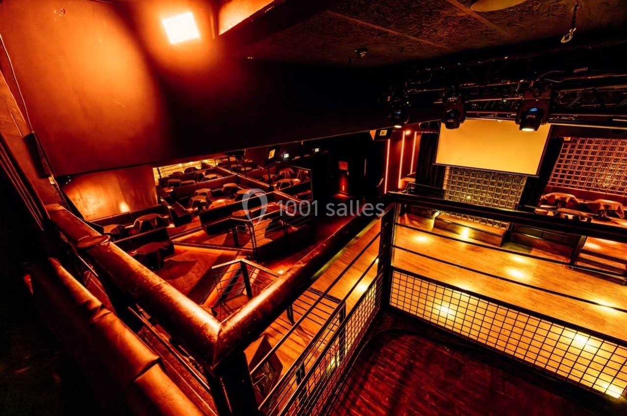 Salle de spectacle avec éclairage chaleureux, sièges disposés en gradins et scène équipée d'un écran.