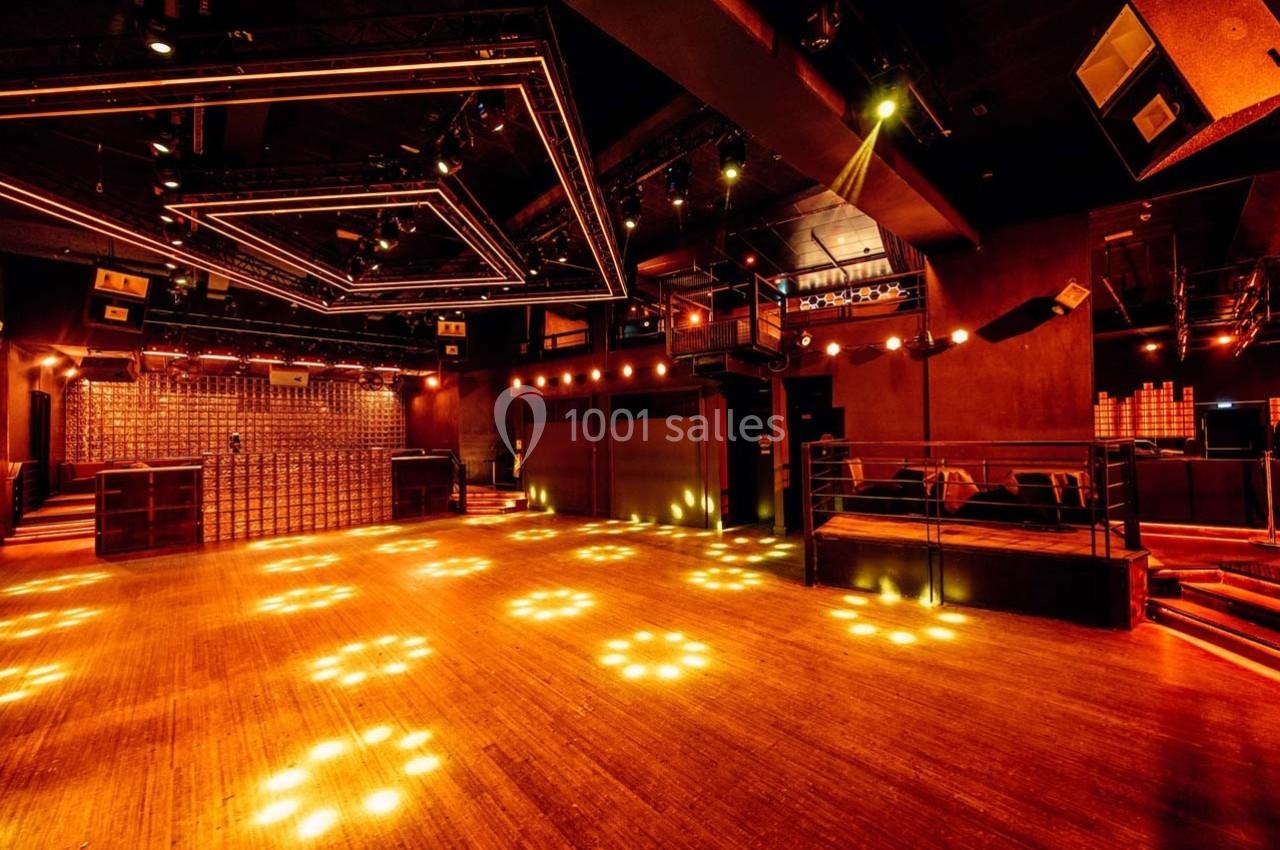 Salle de concert vide avec éclairage chaleureux, parquet en bois et structures lumineuses au plafond.