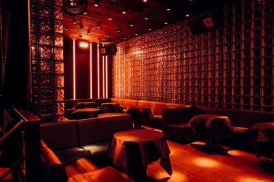 Salle de club vide avec éclairage tamisé, tables rondes, banquettes et escalier menant à une piste de danse.