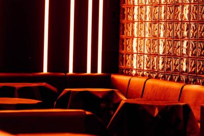 Salle de club vide avec éclairage tamisé, tables rondes, banquettes et escalier menant à une piste de danse.