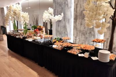 Buffet élégant avec plats variés disposés sur des tables noires, décoré de fleurs blanches dans une salle lumineuse.