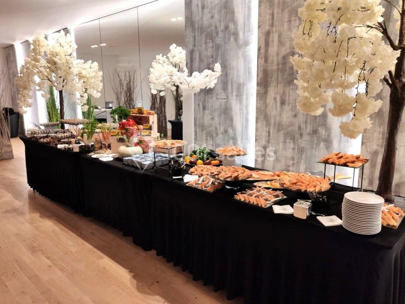 Buffet élégant avec une variété de plats, fruits et desserts, disposé sur une longue table noire, décorée d'arbres blancs.