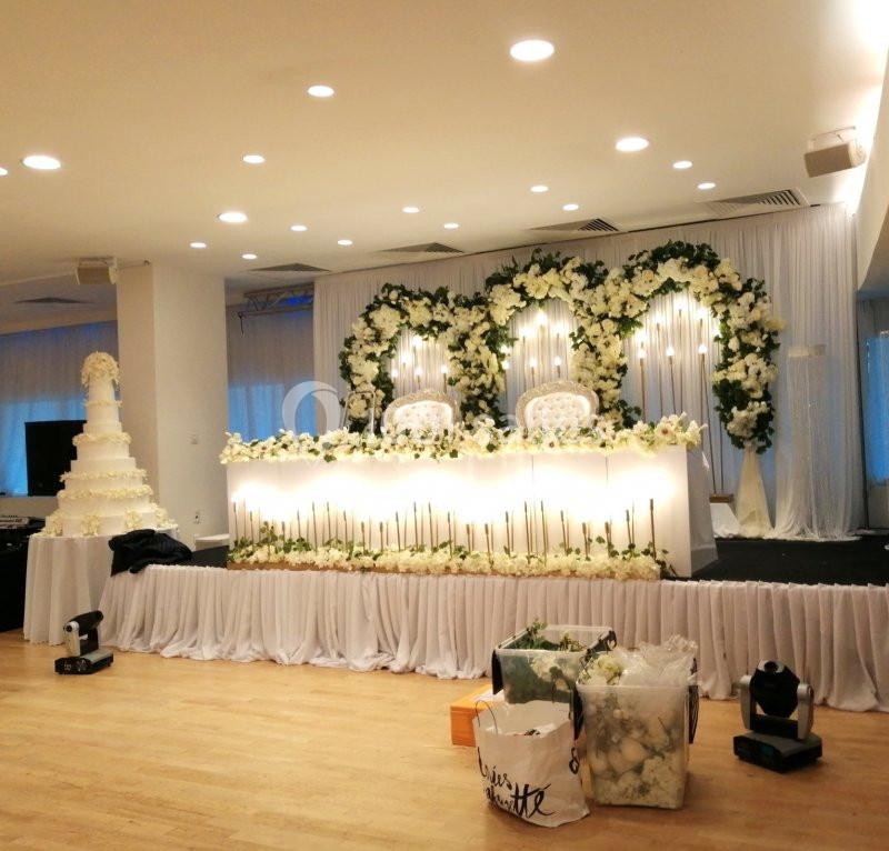 Décoration de salle de réception avec arche florale blanche, table ornée et gâteau de mariage à plusieurs étages.