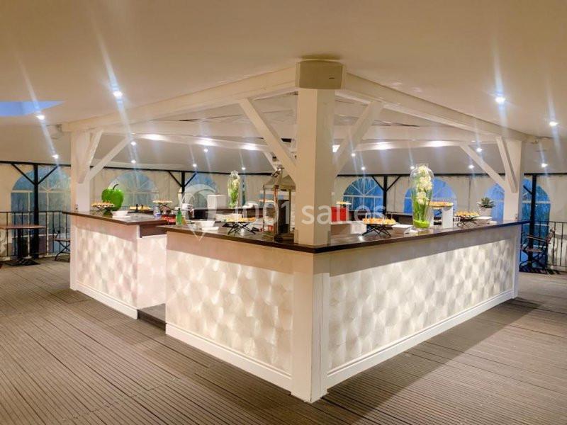 Comptoir central en bois blanc dans une salle lumineuse, entouré de décorations et de tables dressées.