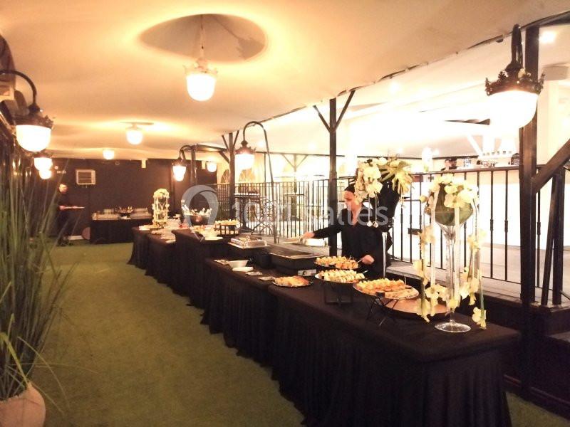 Buffet élégant avec plats variés disposés sur des tables noires, décoré de fleurs blanches dans une salle lumineuse.