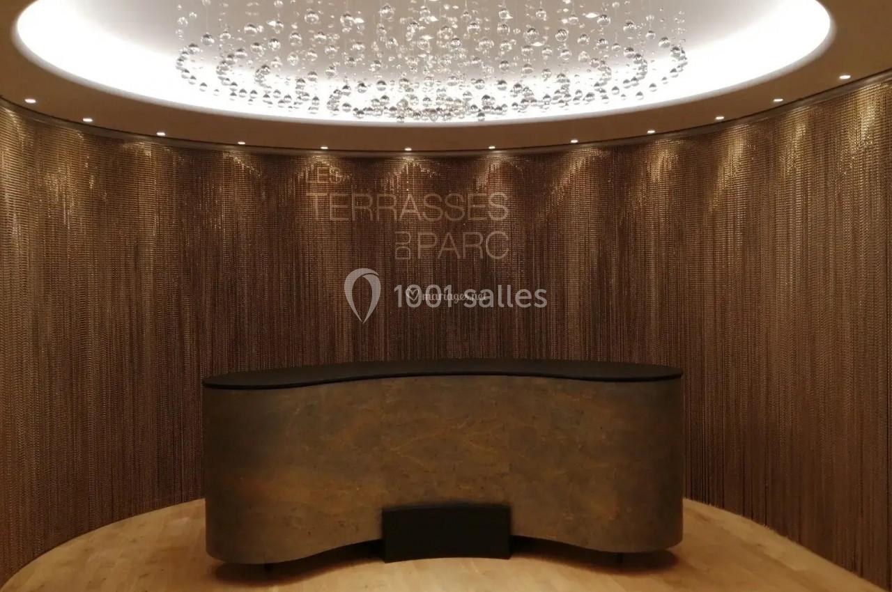 Comptoir en pierre devant un mur texturé avec rideaux métalliques et lustre moderne suspendu.