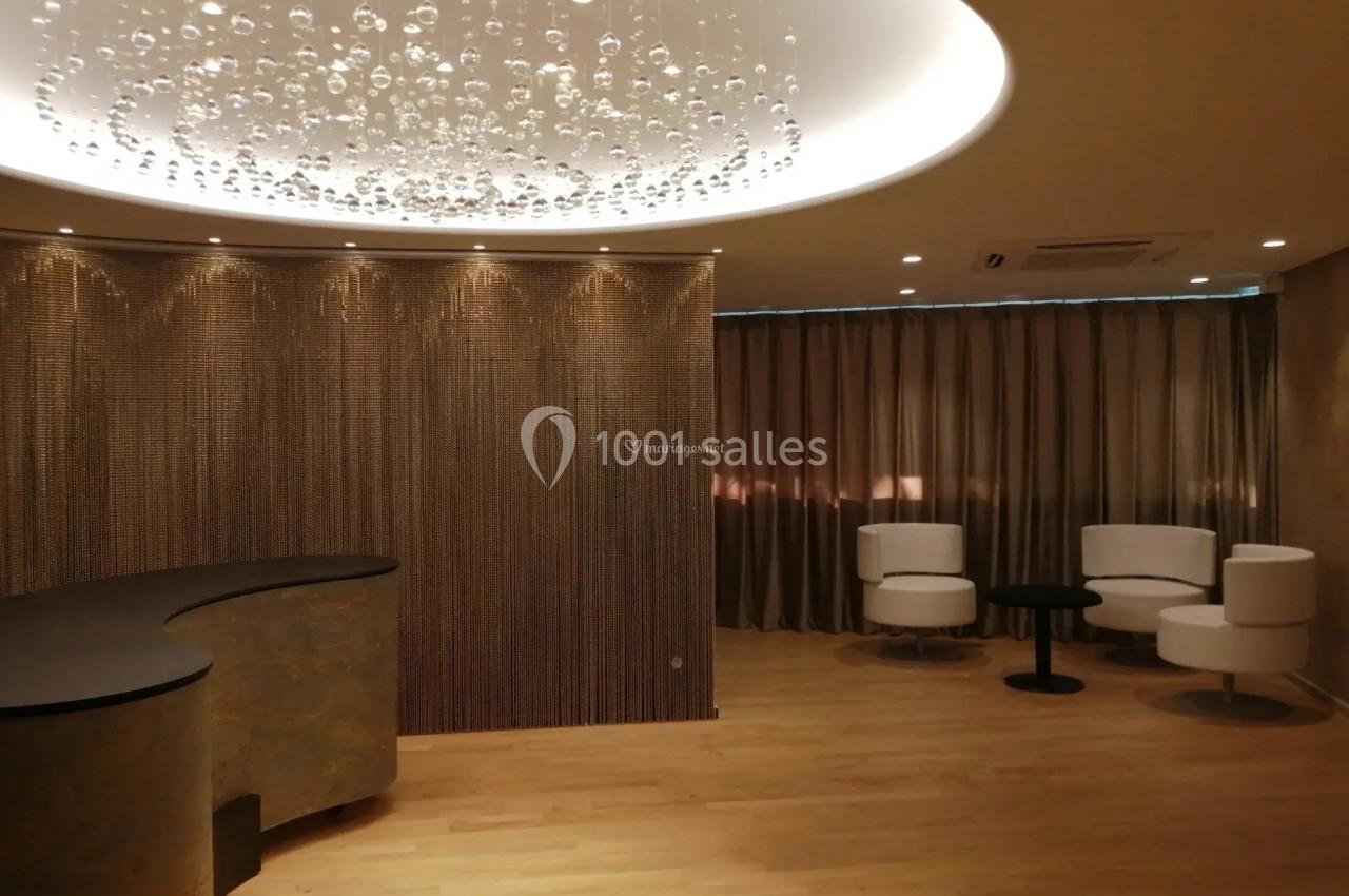 Salle d'attente moderne avec un comptoir courbé, des fauteuils blancs, un rideau beige et un plafond éclairé.