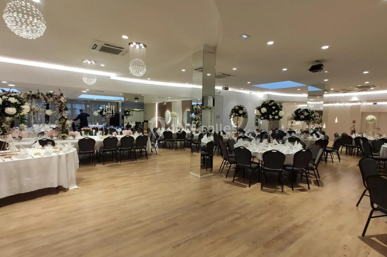 Salle de réception élégante avec tables dressées, décorations florales et éclairage lumineux.