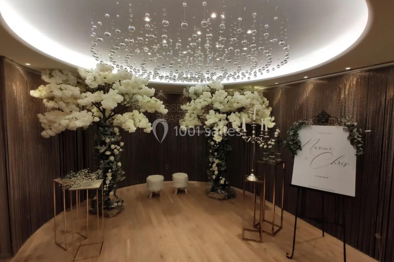 Salle décorée avec des arbres artificiels blancs, un panneau d'accueil et un éclairage suspendu élégant.