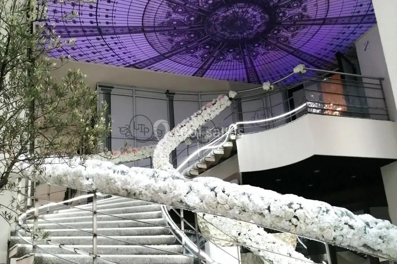 Escalier décoré de fleurs blanches sous une verrière violette ornée de motifs géométriques.