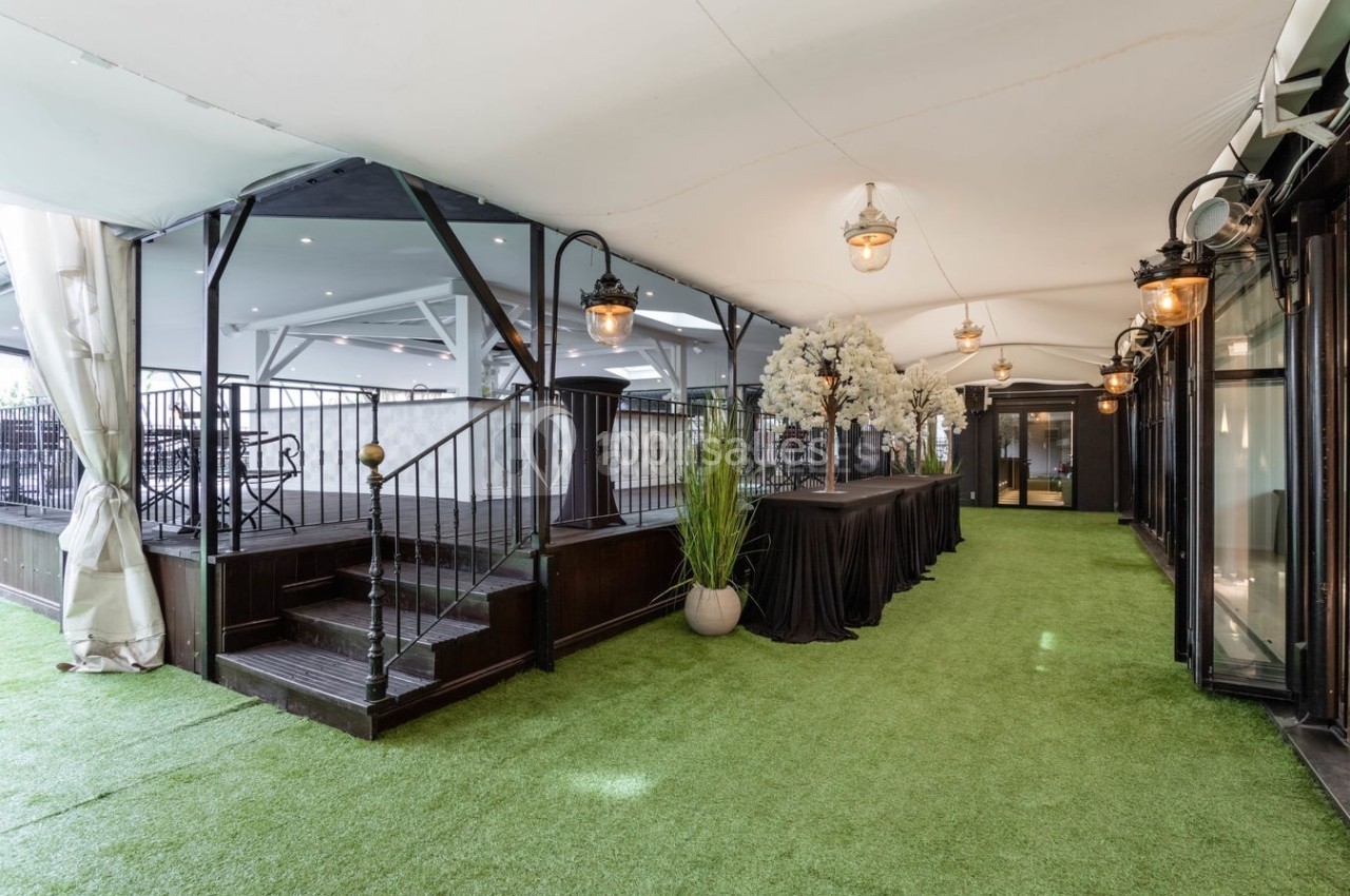 Espace intérieur avec sol en gazon synthétique, escalier en bois, table décorée de fleurs blanches et lampes suspendues.