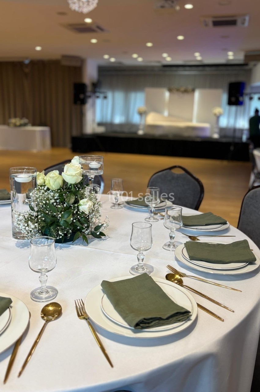 Table dressée avec une nappe blanche, couverts dorés, serviettes vertes et un centre de table floral dans une salle de…