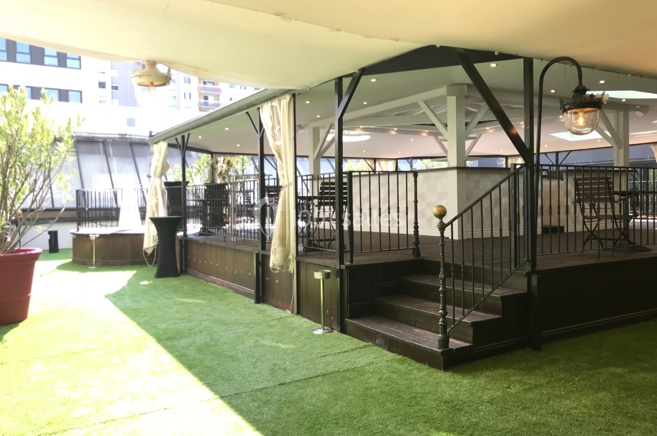 Terrasse couverte avec sol en gazon synthétique, tables et chaises sous une structure en bois et métal.
