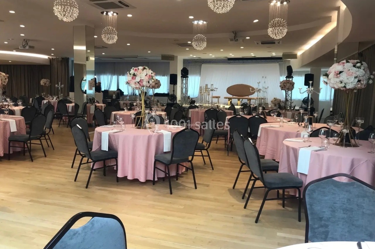 Salle de réception élégante avec tables rondes dressées, nappes roses et décorations florales sur supports dorés.